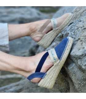Alpargata cuña media pasamaneria empeine de AnseRioja azul o beige puestas en los pies sobre una roca en la playa