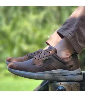 Zapatos Skechers Glavine impermeables marrón en perfil lateral, puestos con pantalones marrones en un parque.