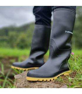 Hombre en el campo usando botas de agua Vikinga negras de Dunlop, ideales para trabajos en ambientes húmedos