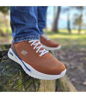 Deportivo hombre Skechers Arch marron puestas en un hombre posando sobre un tronco talado.