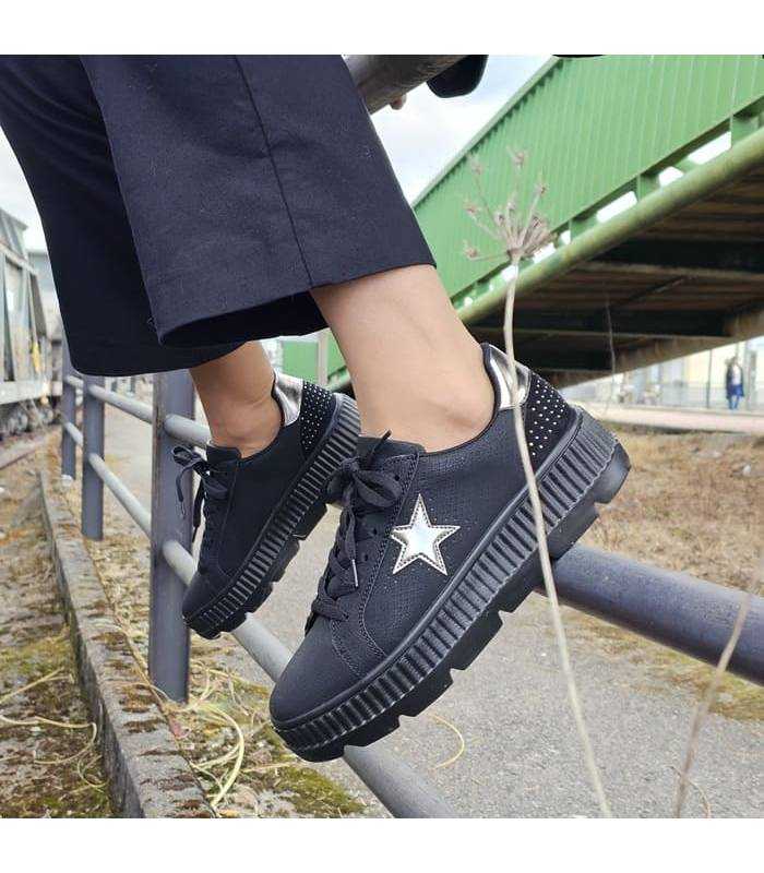 Sneakers mujer negro plataforma ligera de Wuapas puesto en los pies apoyados en una barandilla