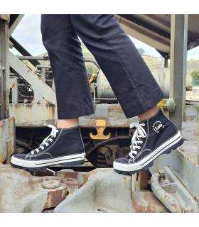 Bota negra de lona puesta en modelo posando entre dos vagones de tren
