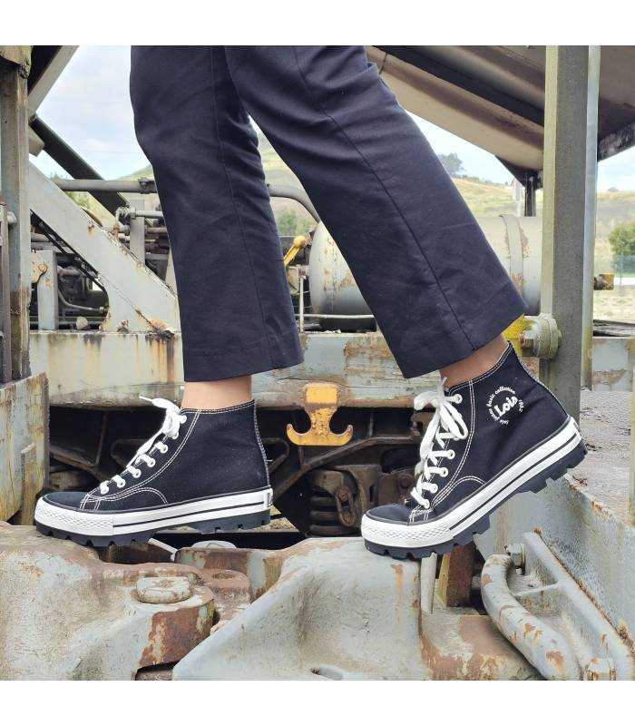 Bota negra de lona puesta en modelo posando entre dos vagones de tren