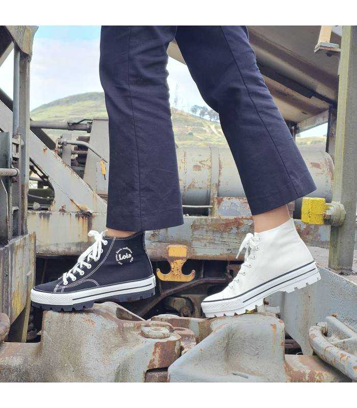 Bota de lona deportiva blanca y negra, una puesta en cada pié.