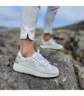 Mujer posando sobre unas rocas junto al mar con los zapatos de piel blanca con cordones de Suave by Leyland.