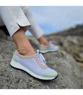 modelo posando sobre rocas junto al mar con los zapatos blancos con detalles en rosa y verde de Suave by Leyland