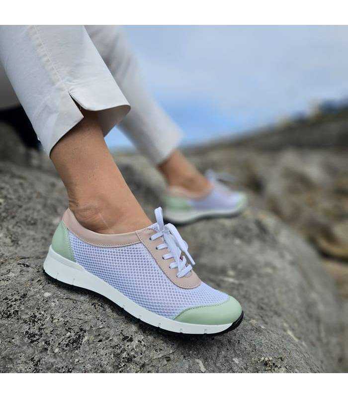 modelo posando sobre rocas junto al mar con los zapatos blancos con detalles en rosa y verde de Suave by Leyland