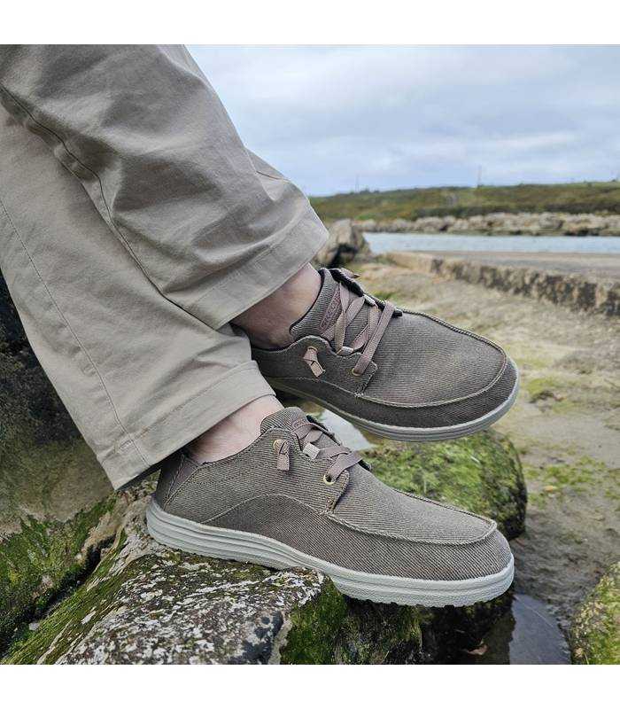 Pies cruzados de un hombre en una roca posando con los zapatos deportivos Melson beige de Skechers