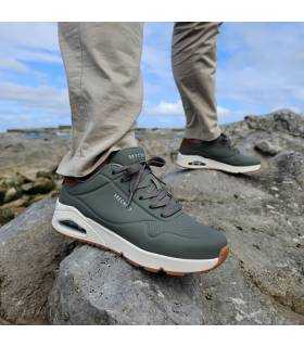 Hombre posando sobre rocas con las zapatillas deportivas verdes Suited de Skechers