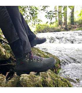hombre posnado sentado junto al rio con las botas Xacobeo azules puestas