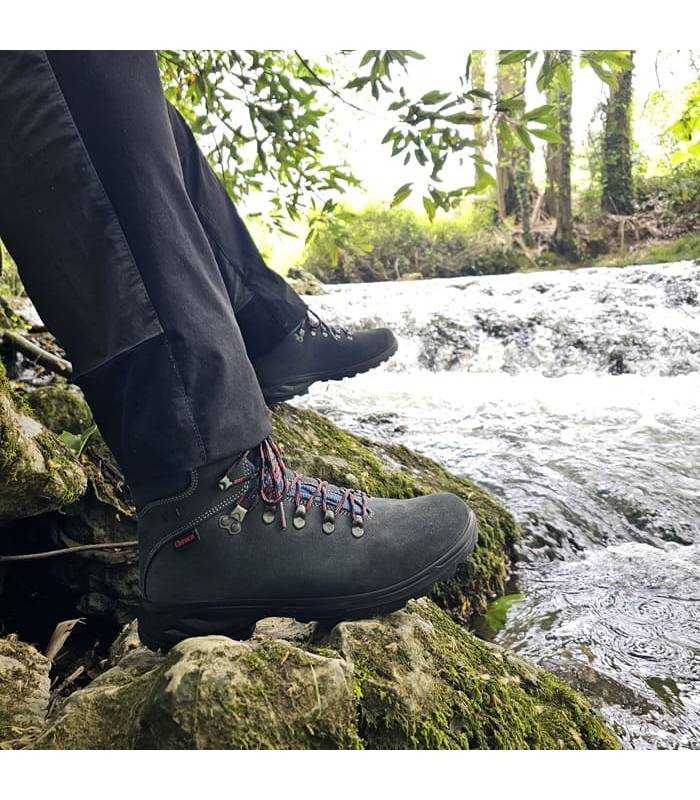 hombre posnado sentado junto al rio con las botas Xacobeo azules puestas