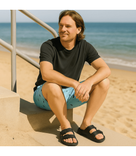 hombre posando en una escalera junto a la playa con las sandalias negras de playa fabricadas por Ncoboco