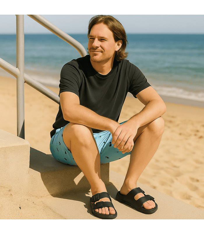 hombre posando en una escalera junto a la playa con las sandalias negras de playa fabricadas por Ncoboco