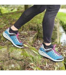 zapatillas trekking mujer azul Grisport puesta caminando por roca con musgo y cordones fucsia