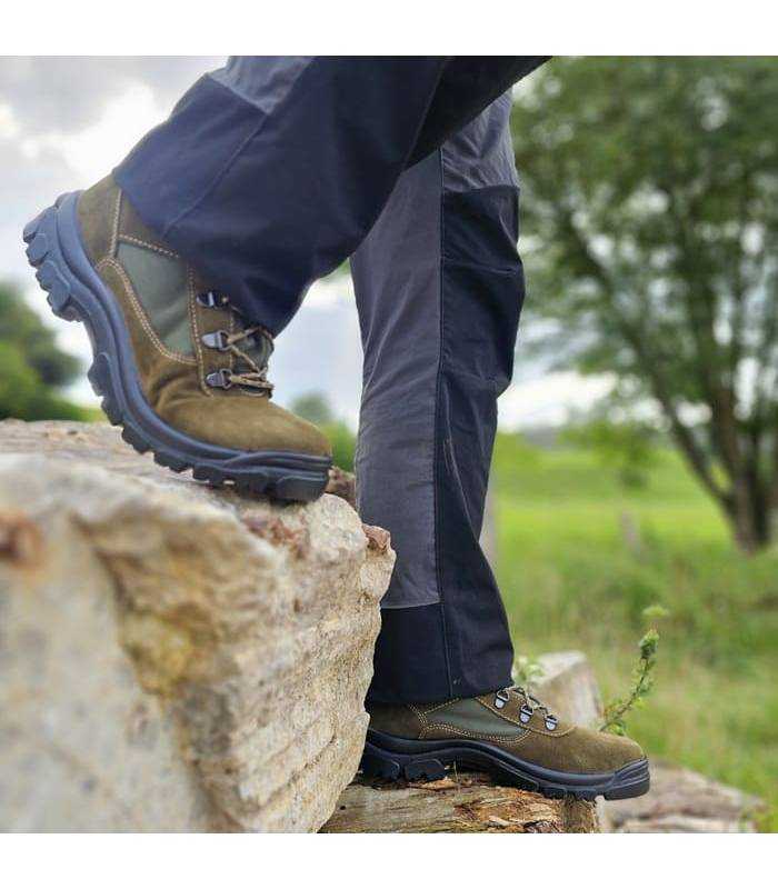 hobre caminando sobre rocas con las botas de senderismo verdes de Postigo