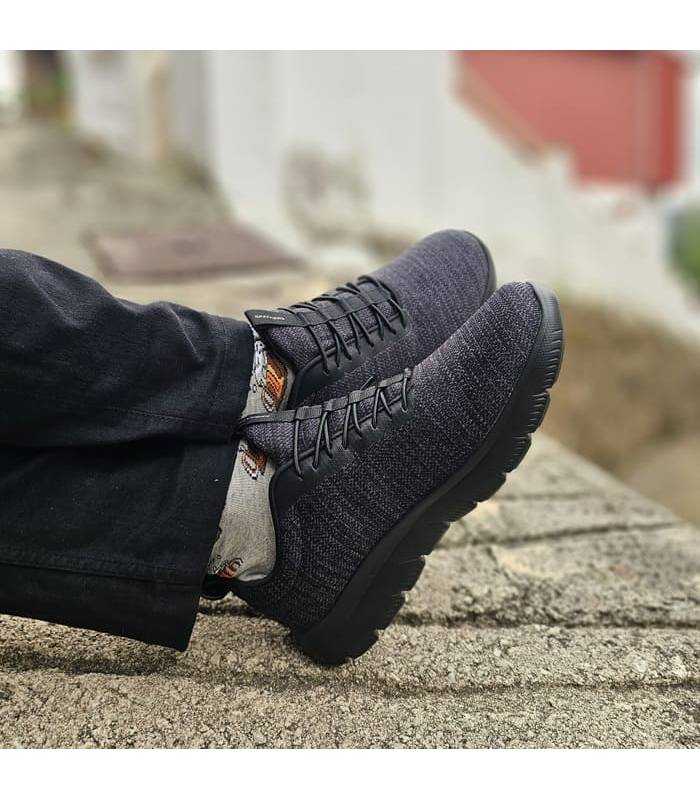 hombre con los pies cruzados sobre un camino emepdrado con las zapatillas negras Summits de Skechers puestas
