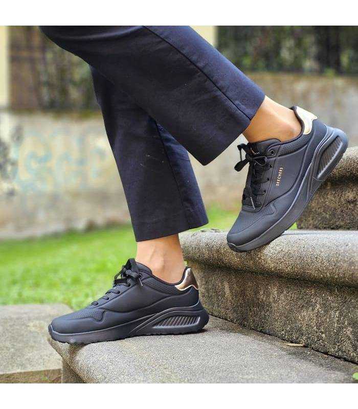 mujer bajando escalaeras con las zapatillas deportivas negras de Skechers puestas