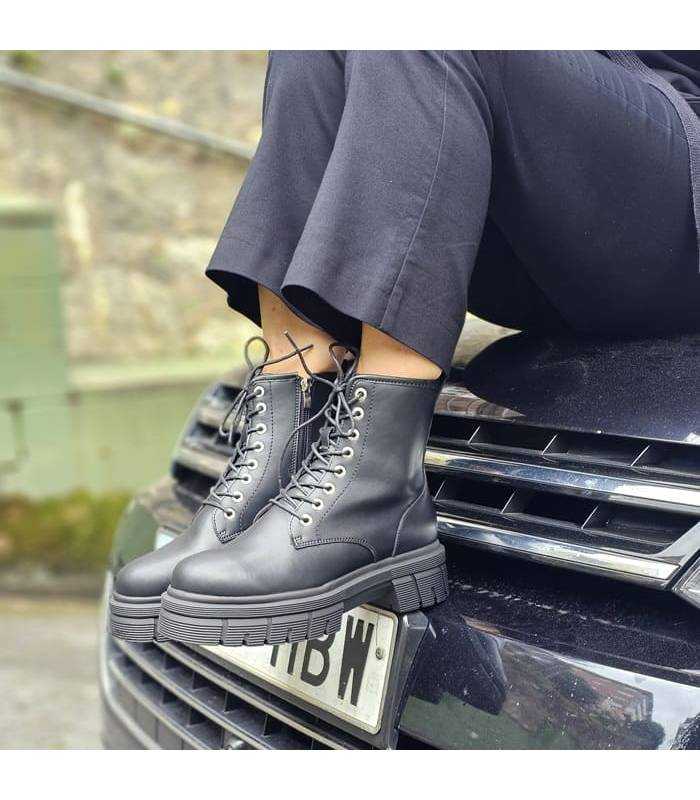 mujer posando encima de un coche con las botas de piel negras tipo militar puestas