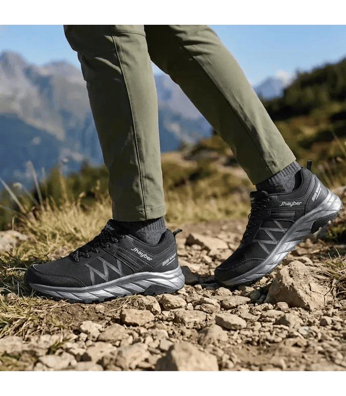 Zapatillas trekking hombre Racosa negras de J’hayber puestas sobre unas rocas